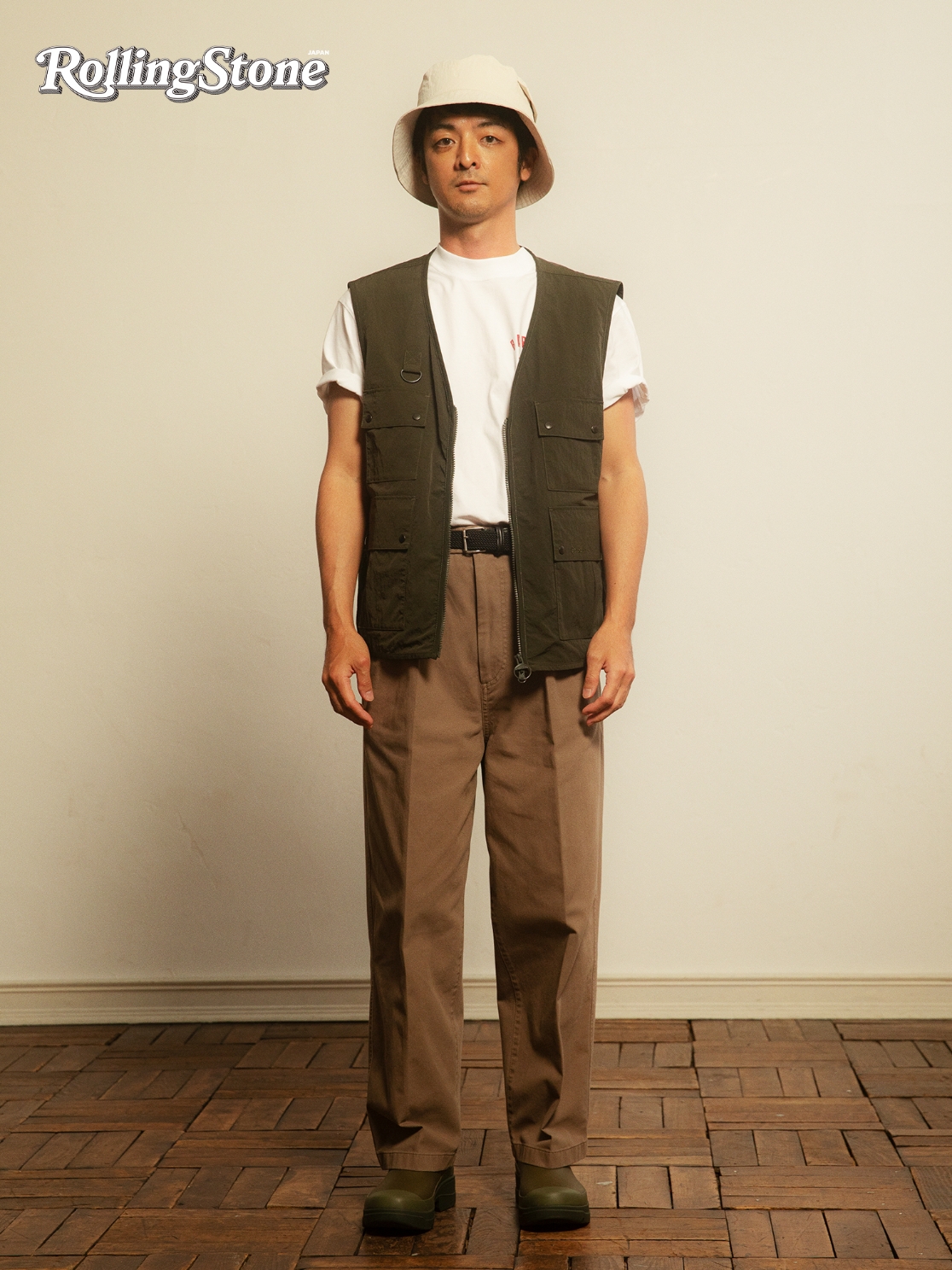 ベージュのバケットハット、白Tシャツにカーキのベスト、茶色のパンツを着用したYAMATOの写真