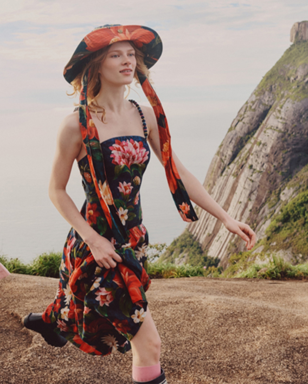 花柄のドレスと帽子を着用し、山を背景に歩く女性を写したコラージュ画像。